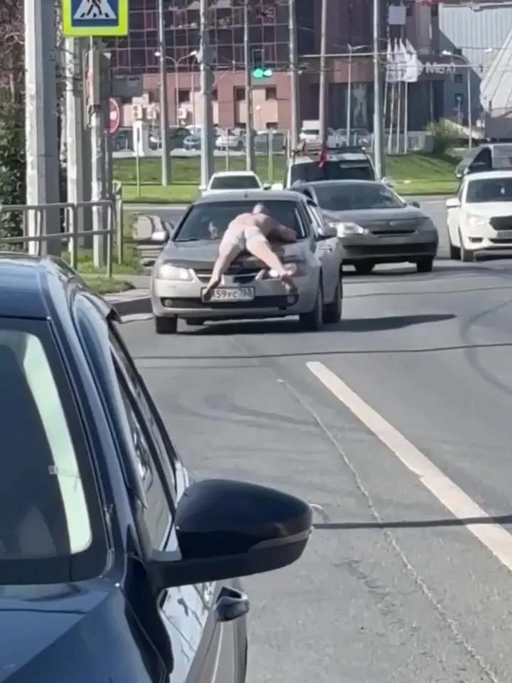 На пересечении улицы Авроры и Московского шоссе прохожие увидели мужчину на капоте автомобиля. Жители выдвигают версии от жары и опьянения до проигрыша в споре.